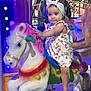 adult_hand, amusement_park, blue_light, carousel, child, colorful, fun, headband, horse, night, outdoor, person, playful, purple_light, ride, romper, smiling, support, toddler, toy