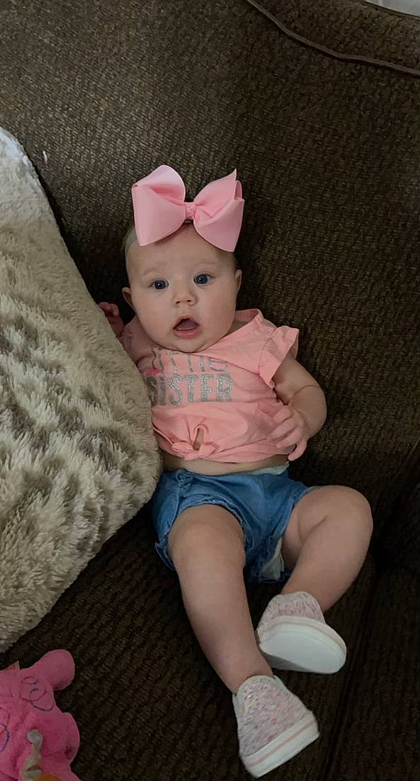 Adley is registered to the contest to win money with this photo: baby, baby_toddler_clothing, cap, comfort, costume_hat, couch, dress, fawn, finger, hat, head, headgear, headwear, human_body, person, pink, skin, sleeve, sock, sun_hat