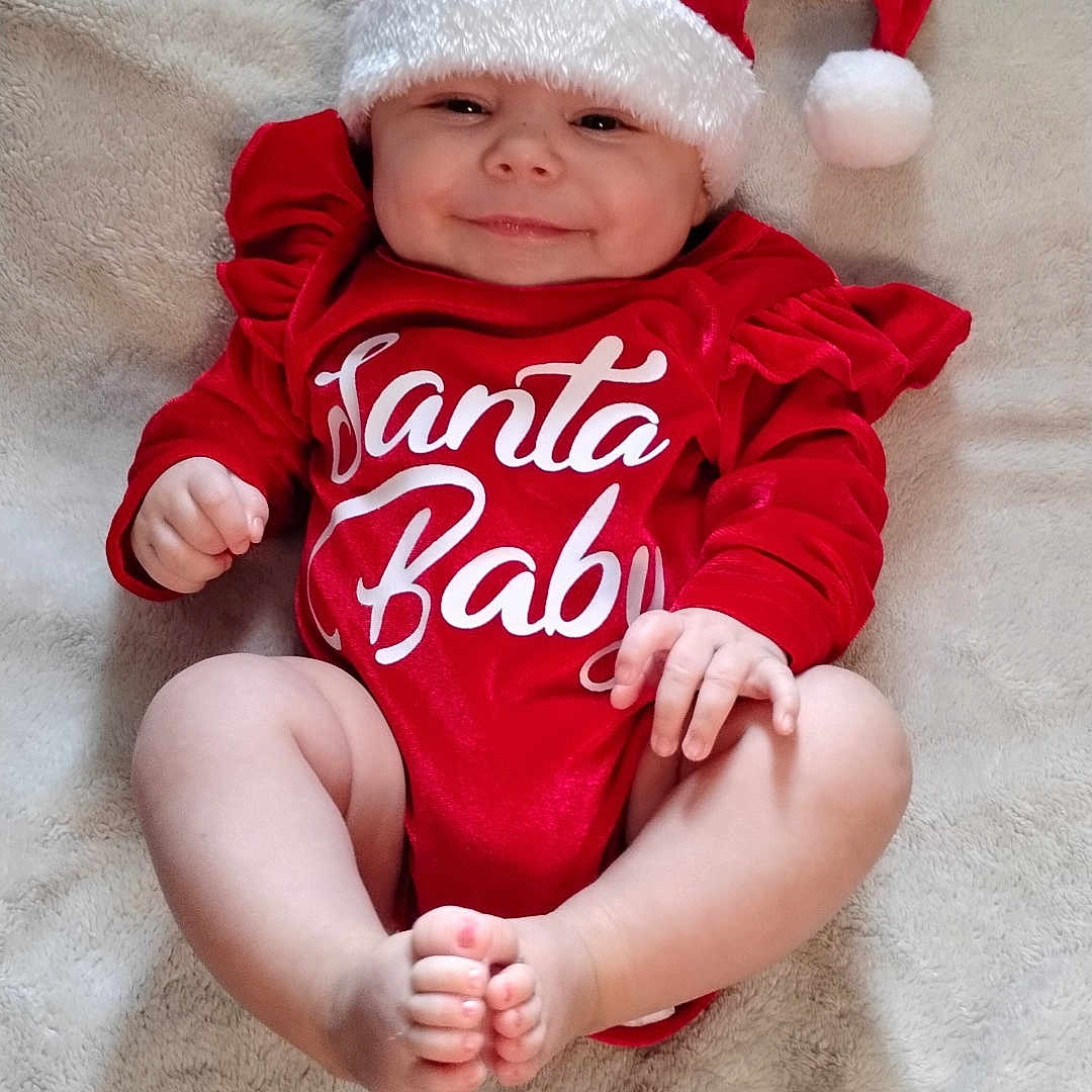 Mattie is registered to the contest to win money with this photo: baby, blanket, child, christmas, cozy, cute, festive, foot, hand, happy, holiday, indoors, infant, lying_down, portrait, red_clothing, santa_hat, skin, smile, soft_texture