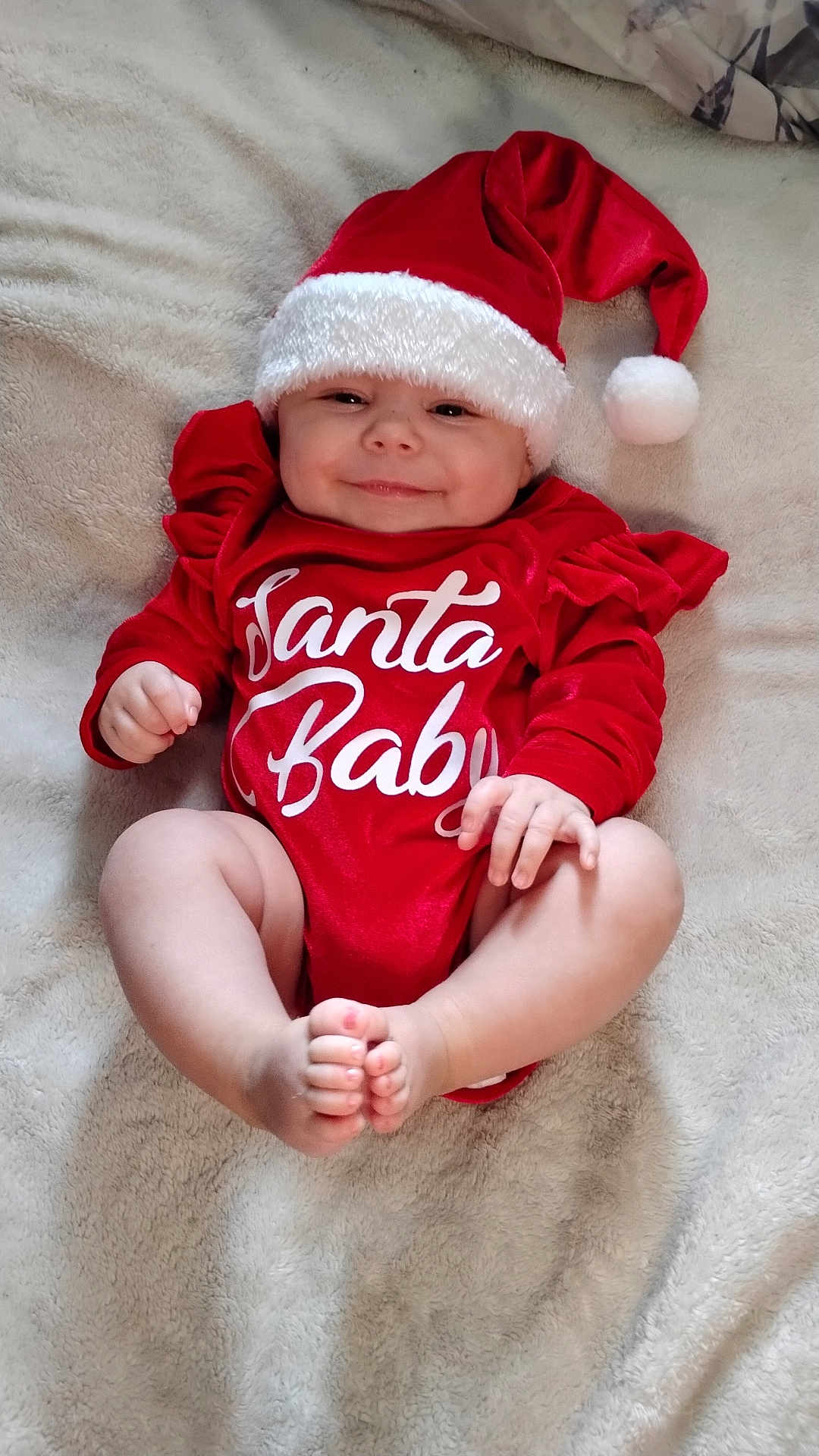 Mattie is registered to the contest to win money with this photo: baby, infant, smile, red_clothing, santa_hat, christmas, holiday, cute, lying_down, blanket, soft_texture, festive, happy, child, skin, hand, foot, indoors, portrait, cozy