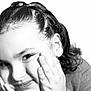 child, face, close_up, portrait, black_and_white, smile, hands_on_face, cheeks, hair, braids, eye, eyebrow, ear, skin, expression, studio_lighting, sweater, playful, cute, monochrome