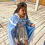child, girl, dress, cape, costume, wooden_floor, shoes, princess, candid, indoor, clothing_rack, dresses, playful, expressive_face, hairclip, sparkly, silver_dress, blue_cape, standing, studio