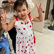 Adele is registered to the contest to win money with this photo: child, girl, white_dress, red_hearts, pearl_necklace, pearl_bracelet, peace_sign, hair_styling, curling_iron, adult, backstage, door, wooden_floor, purse, smile, posing, indoor, chair, footwear, accessory