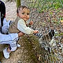 Lino a rejoint le concours — aidez-le/la à gagner de superbes lots ! toddler, child, adult, hand, wire_fence, lemur, animal, outdoor, nature, tree, ground, shoes, clothing, curious, greenery, person, holding, daylight, exploration, wildlife