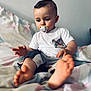 baby, child, toddler, pacifier, barefoot, bed, blanket, white_shirt, shorts, indoor, curly_hair, face, expression, sitting, foot, hand, clothing, young, portrait, light