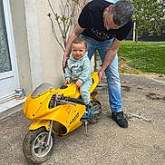 Lino a rejoint le concours — aidez-le/la à gagner de superbes lots ! child, adult, motorcycle, yellow_motorcycle, outdoor, concrete, tree, plant, house, hoodie, jeans, sneakers, smiling, person, toy, daylight, greenery, happy, baby, casual