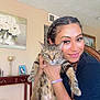 Lily is registered to the contest to win money with this photo: woman, cat, indoor, smiling, braids, tabby_cat, pet, holding, portrait, furniture, painting, table, home, decor, person, face, animal, happy, seated, relaxed