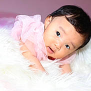 Fandana is registered to the contest to win money with this photo: baby, infant, pink_clothing, fluffy_blanket, soft_texture, portrait, cute, child, young, face, eyes, skin, head, laying_down, indoors, cozy, curious, closeup, warm, adorable
