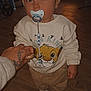 child, toddler, pacifier, beanie, sweater, lion_king, hand, tattoo, wooden_floor, toy, shoes, pants, indoor, living_room, sofa, portrait, person, pacifier_clip, gaze, cozy