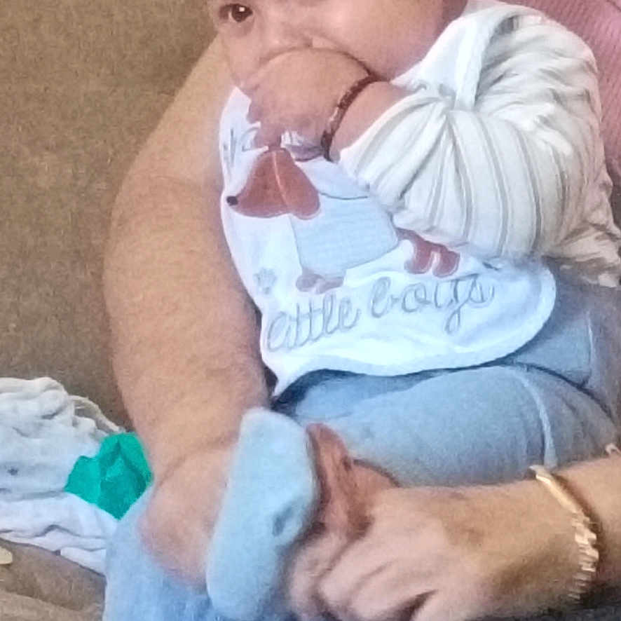 Akira is registered to the contest to win money with this photo: baby, beanie, bib, blue_clothing, couch, cute, face, hand, infant, leg, person, sitting, sock, thumb_in_mouth, toy, toddler, wearing, warm_clothing, adult, indoor