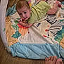 baby, child, playing, play_mat, green_clothing, floor, wooden_floor, animal_prints, toes, curious, infant, indoors, crawling, colorful, person, smiling, looking_up, home, young_child, cute