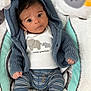 baby, infant, blue_hoodie, striped_pants, cushion, plush_toy, knitwear, face, wide_eyes, curious, cute, child, indoor, soft_texture, patterned_background, newborn, lying_down, casual_clothing, small_hands, adorable