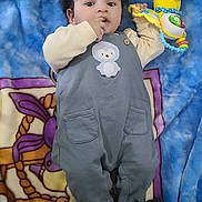 Younes a rejoint le concours — aidez-le/la à gagner de superbes lots ! baby, child, toy, yellow_duck, striped_socks, grey_onesie, penguin_patch, blanket, colorful, indoor, lying_down, cute, infant, face, hand, expression, soft_toy, clothing, footwear, person