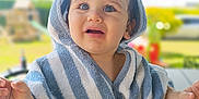 Liâm a rejoint le concours — aidez-le/la à gagner de superbes lots ! baby, blue_and_white, blurred_background, child, curious_expression, daylight, drool, face, greenery, hooded_towel, outdoor, person, playground, portrait, striped_towel, summer, sunlight, toddler, wooden_table, young_child