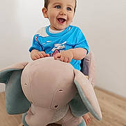 Liâm participe au concours pour gagner de l'argent avec cette photo : baby_clothes, blue_eyes, bright, child, cute, elephant, furniture, happy, indoor, minimalist, person, playtime, plush_toy, rocking_toy, short_hair, sitting, smiling, toddler, toy, wooden_floor