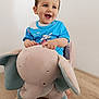 baby_clothes, blue_eyes, bright, child, cute, elephant, furniture, happy, indoor, minimalist, person, playtime, plush_toy, rocking_toy, short_hair, sitting, smiling, toddler, toy, wooden_floor
