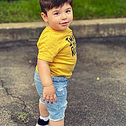 Imran is registered to the contest to win money with this photo: child, toddler, boy, portrait, outdoor, standing, smiling, yellow_shirt, denim_shorts, sneakers, black_shoes, white_socks, pavement, sidewalk, grass, park, fashion, street_style, short_hair, full_body