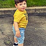 child, toddler, boy, portrait, outdoor, standing, smiling, yellow_shirt, denim_shorts, sneakers, black_shoes, white_socks, pavement, sidewalk, grass, park, fashion, street_style, short_hair, full_body