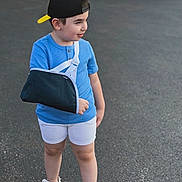 Imran joined the competition — help win amazing prizes! child, boy, outdoor, portrait, standing, blue_shirt, baseball_cap, backward_cap, arm_sling, injured_arm, shorts, sandals, pavement, street, road, greenery, daylight, profile, casual_clothing, person