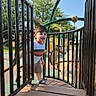 boy, casual_clothing, child, climbing, outdoor, park, play_structure, playground, portrait, railings, shorts, smiling, sneakers, stairs, standing, striped_shirt, summer, sunlight, toddler, trees