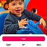 blue_toy, boy, brown_hair, casual_clothing, child, colorful_background, dark_sweater, face, happy, indoor, looking_at_camera, play_area, playground, portrait, ride_on_toy, screenshot, seated, smiling, toddler, vote_button