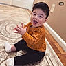 black_pants, carpet, child, hands, happy, home, indoor, laughing, open_mouth, orange_shirt, photography, playful, portrait, rug, short_hair, sitting, smiling, toddler, white_socks, wood_floor