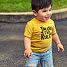 child, toddler, boy, smiling, outdoor, portrait, yellow_shirt, denim_shorts, ripped_clothing, standing, playful, happy, face, hair, grass, pavement, street, daylight, casual_fashion, text_on_shirt
