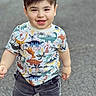 child, boy, toddler, smiling, portrait, standing, indoors, dinosaur_shirt, colorful_clothing, short_hair, brown_hair, face, eyes, teeth, happy, casual_clothing, shorts, gray_background, full_body, photography