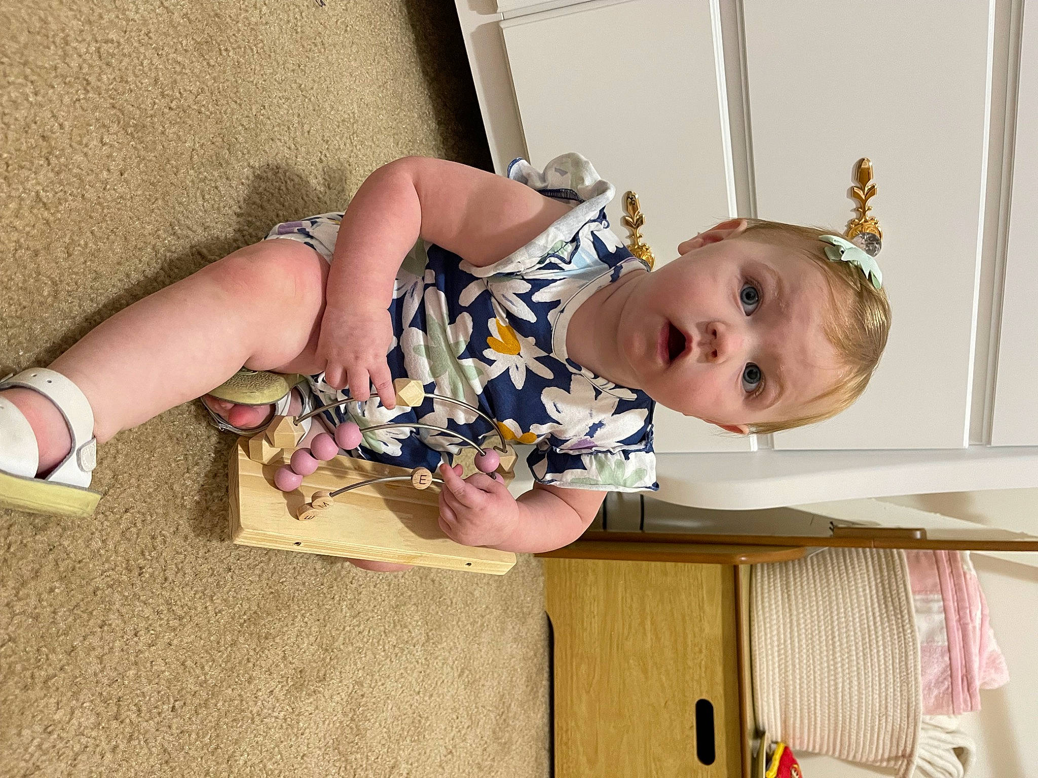 Emery is registered to the contest to win money with this photo: baby, baby_products, baby_toddler_clothing, child, comfort, dress, eye, flooring, foot, fun, happy, human_leg, pattern, person, room, sitting, surprise, thigh, toddler, wood