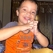 Lukas joined the competition — help win amazing prizes! child, boy, smile, hands, orange_shirt, mustard_pants, indoor, curtains, fan, happy, person, face, sitting, casual_clothing, playful, young, portrait, home, expression, cute
