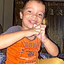 child, boy, smile, hands, orange_shirt, mustard_pants, indoor, curtains, fan, happy, person, face, sitting, casual_clothing, playful, young, portrait, home, expression, cute