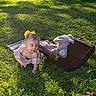 child, toddler, baby, outdoor, grass, sunlight, portrait, crawling, curious, smiling, yellow_bow, dress, teddy_bear, stuffed_animal, suitcase, vintage, picnic, nature, playful, photography