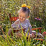 child, toddler, girl, portrait, outdoor, garden, chair, yellow_bow, floral_dress, flower, coneflower, grass, plants, foliage, nature, sunlight, sitting, smiling, barefoot, wooden_chair