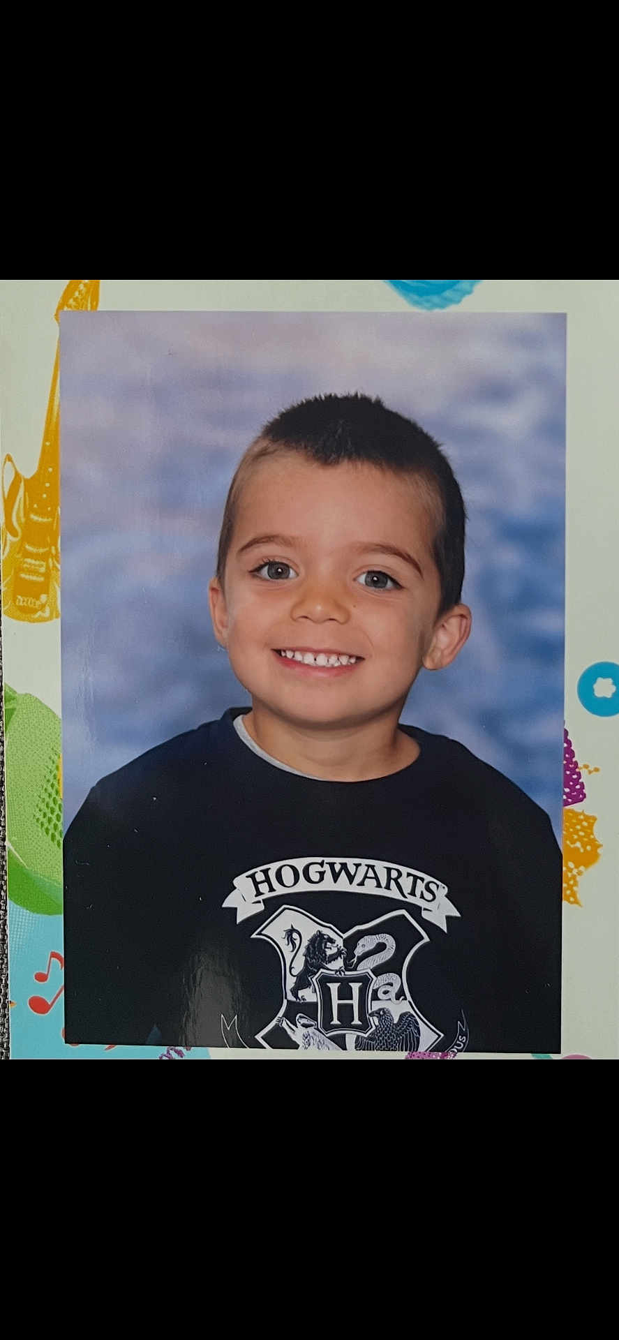 Charly participe au concours pour gagner de l'argent avec cette photo : child, boy, smiling, school_portrait, hogwarts_logo, t_shirt, short_hair, teeth, blue_background, studio_photo, face, eyes, ears, portrait, kid, young_child, happy, centered, indoors, photo_print