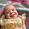 baby, infant, smile, tongue_out, face, blanket, patterned_blanket, colorful, cute, happy, clothing, yellow_outfit, closeup, portrait, child, young, skin, head, eyes, expression
