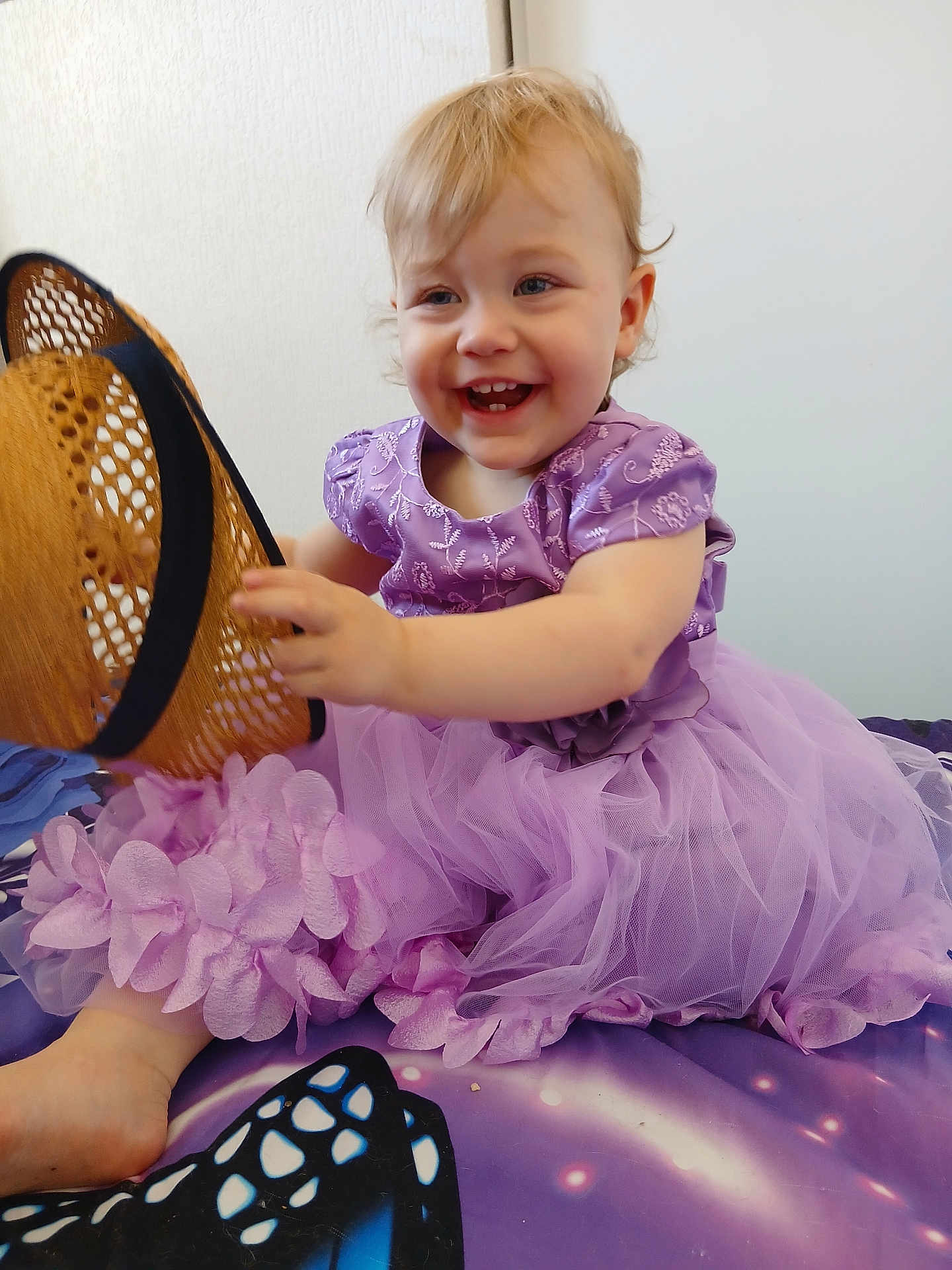 Elysianna participe au concours pour gagner de l'argent avec cette photo : toddler, child, smiling, purple_dress, hat, sitting, indoors, happy, cute, playful, face, person, foot, flower_detail, fabric, toy, pattern, colorful, young_child, blonde_hair