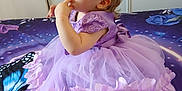 Elysianna participe au concours pour gagner de l'argent avec cette photo : toddler, child, dress, lavender, bedspread, butterfly, curious, finger_in_mouth, sitting, indoor, portrait, young_child, cute, clothing, fabric, person, baby, furniture, colorful, pattern