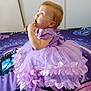 toddler, child, dress, lavender, bedspread, butterfly, curious, finger_in_mouth, sitting, indoor, portrait, young_child, cute, clothing, fabric, person, baby, furniture, colorful, pattern