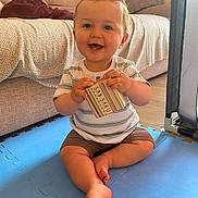 Andrea participe au concours pour gagner de l'argent avec cette photo : baby, child, smiling, indoor, play_mat, box, striped_shirt, shorts, barefoot, couch, pillow, floor, wooden_floor, happy, sitting, person, toddler, home, toy, cute