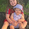 child, baby, sibling, sitting, smiling, outdoor, tree, grass, blanket, portrait, family, infant, toddler, hat, dress, red_clothing, checkered_pattern, summer, cuddling, sunlight
