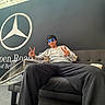 Zarco joined the competition — help win amazing prizes! person, cat, kitten, sitting, couch, sofa, sunglasses, peace_sign, fashion, casual_clothing, gray_sweatshirt, black_pants, indoor, automotive_showroom, mercedes_logo, brand_sign, car_display, portrait, pet, relaxed