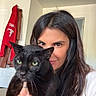 woman, cat, black_cat, indoor, portrait, long_hair, green_eyes, holding, door, clothing, red_hoodie, hand, tattoo, face, looking, pet, animal, cozy, casual, home