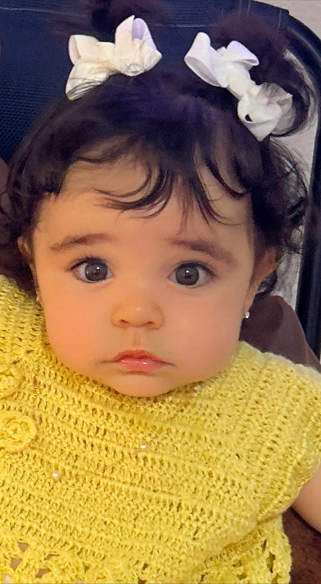 Aisha is registered to the contest to win money with this photo: child, toddler, face, eyes, hair_bows, curly_hair, yellow_clothing, knitted_top, portrait, cute, baby, indoor, person, young_child, closeup, expression, sitting, earrings, fashion, adorable