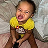 Kiara joined the competition — help win amazing prizes! baby, child, toddler, portrait, smiling, funny_expression, facial_expression, curly_hair, yellow_shirt, hairbrush, bed, bedding, blanket, pillow, indoors, sitting, playful, closeup, person, photograph