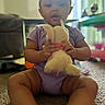 baby, child, toddler, plush_toy, bunny, stuffed_animal, sitting, carpet, indoors, playroom, purple_clothing, onesie, portrait, closeup, facial_expression, open_mouth, hands, toy, home, natural_light