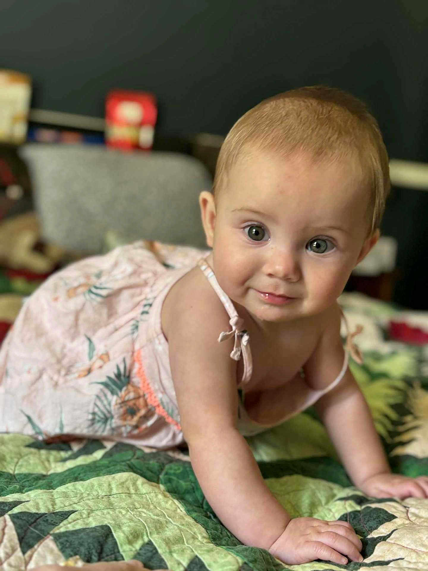 Marielle is registered to the contest to win money with this photo: baby, child, crawling, dress, quilt, indoor, curious, cute, infant, person, young_child, smiling, skin, face, hand, green, pattern, bedroom, home, portrait