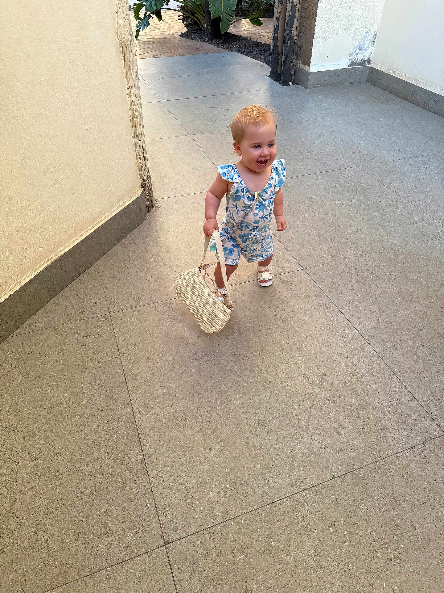 Amara-May is registered to the contest to win money with this photo: toddler, child, smiling, romper, handbag, footwear, sandals, hair, walking, corridor, floor_tiles, wall, outdoor, daylight, person, cute, happy, fashion, small_bag, baby
