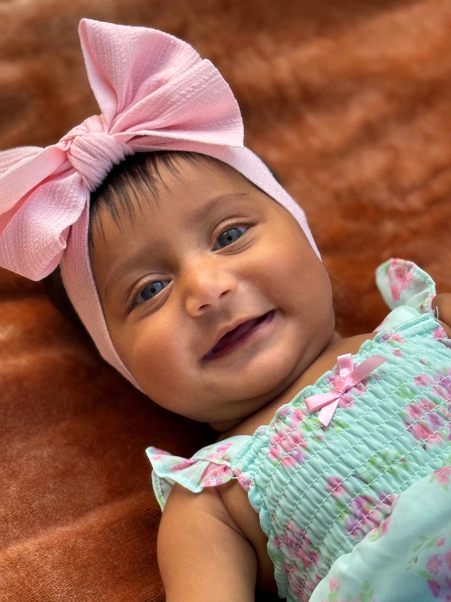 Aleezay is registered to the contest to win money with this photo: baby, child, infant, smile, face, headband, pink_bow, blue_eyes, dress, floral_pattern, pastel_colors, cute, lying_down, soft_blanket, close_up, portrait, happy, skin, person, adorable