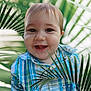 baby, child, smiling, face, portrait, plaid_shirt, blue, green, outdoor, nature, leaf, palm_leaf, happy, cute, young, person, toddler, closeup, eyes, expression