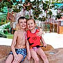 child, children, smiling, water_park, life_vest, swimwear, rock, slide, greenery, outdoor, happy, friendship, summer, playful, barefoot, fun, water, nature, posing, sitting